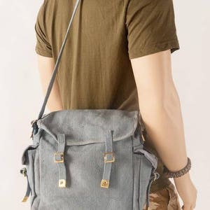 May include: A gray canvas messenger bag with adjustable straps and metal buckles. The bag has a flap closure and a zippered pocket on the front.