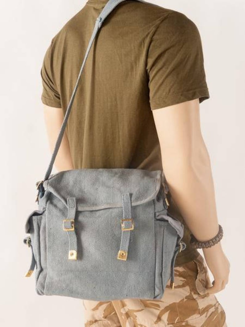 May include: A gray canvas messenger bag with adjustable straps and metal buckles. The bag has a flap closure and a zippered pocket on the front.