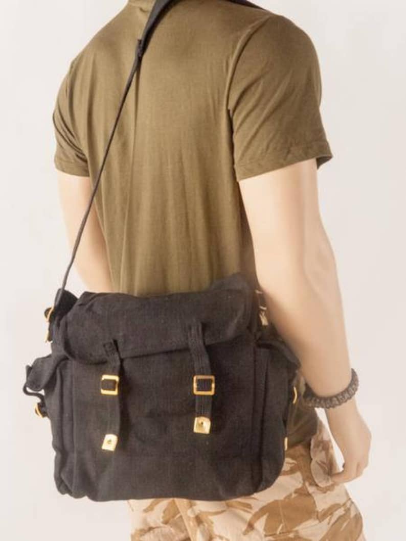 May include: A black canvas messenger bag with gold buckles and a long adjustable strap. The bag has a flap closure and a large main compartment.