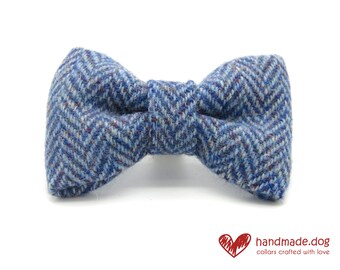 May include: A blue tweed dog bow tie with a herringbone pattern. The bow tie is a light blue with darker blue and red flecks. The text "handmade.dog collars crafted with love" is in the bottom right corner.