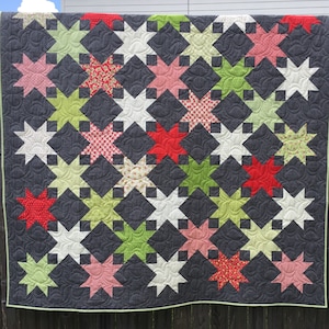 Pode incluir: Uma colcha com um design de patchwork que apresenta uma variedade de cores, incluindo vermelho, rosa, verde, branco e cinza. A colcha é feita de quadrados com estrelas no centro. As estrelas são todas de diferentes cores e padrões.