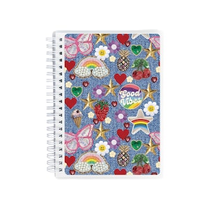 May include: A spiral-bound notebook with a denim-like cover adorned with colorful patches. The patches include butterflies, rainbows, stars, hearts, flowers, and the words "Good Vibes". The notebook has a white spiral binding.