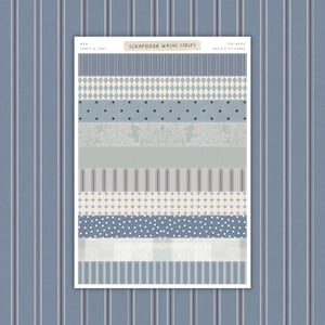 May include: A sheet of scrapbook washi strips in shades of blue, gray, and white. The strips feature various patterns, including stripes, polka dots, diamonds, and floral designs. Text on the sheet reads "SCRAPBOOK WASHI STRIPS" and "COMFY & COZY".