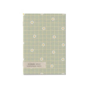 Peut inclure: Un carnet avec un motif de grille vert clair et des illustrations de marguerites blanches. Le texte "BLOOMING BASICS SCRAPBOOKING PAPERS" est imprimé sur une étiquette crème. Le carnet est rectangulaire et a une esthétique pastel douce.