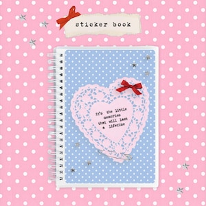 May include: A spiral-bound sticker book with a blue polka-dot cover featuring a pink heart doily design and a red bow. The text "it's the little memories that will last a lifetime" is printed on the heart. The words "sticker book" are written at the top.