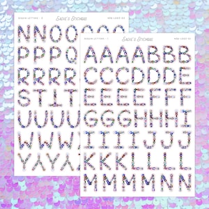 May include: Two sheets of alphabet stickers with sequin letters. The stickers are in various colors and feature the text "Sadie's Stickers" at the top. The letters are outlined in a clear material. The background is a shimmering, iridescent pink and purple.