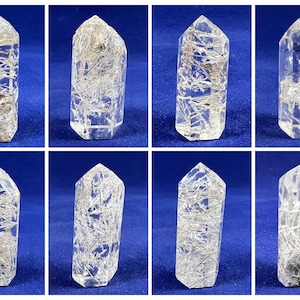 May include: Eight clear quartz crystal points with inclusions of black and silver rutile. The points are all approximately the same size and shape, and they are arranged in two rows of four.
