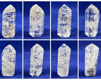 Puede incluir: Ocho puntas de cristal de cuarzo transparente con inclusiones de rutilo negro y plateado. Las puntas son todas aproximadamente del mismo tamaño y forma, y están dispuestas en dos filas de cuatro.