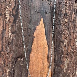 May include: A delicate silver-toned chain necklace featuring a series of small, uniform circular links connected in a continuous pattern. The chain is thin and lightweight, displaying a metallic sheen that reflects light along its entire length.