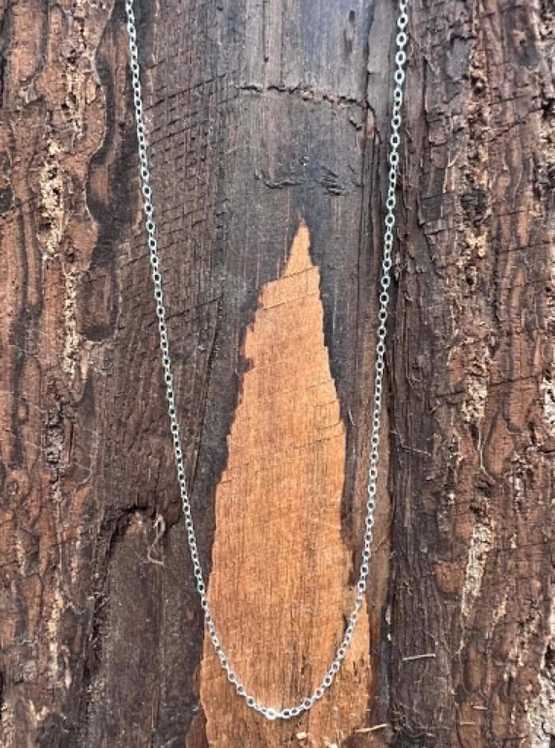 May include: A delicate silver-toned chain necklace featuring a series of small, uniform circular links connected in a continuous pattern. The chain is thin and lightweight, displaying a metallic sheen that reflects light along its entire length.
