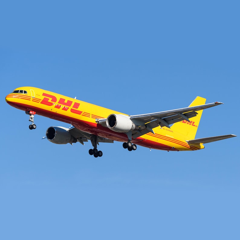 May include: A yellow and red DHL Boeing 757-200F cargo plane in flight against a clear blue sky.