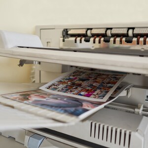 May include: A white printer with a photo collage being printed. The photo collage is a collection of smaller photos arranged in a grid pattern. The printer is in a home or office setting.