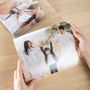 May include: A family of three, a woman, a man, and a young boy, are walking in a park. The woman is wearing a white coat, the man is wearing a white shirt, and the boy is wearing a black jacket and blue jeans. The boy is being held up in the air by his parents.