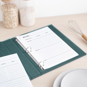 May include: A dark teal three-ring binder containing white recipe pages with printed headers for preparation time, cook time, servings, ingredients, directions, and notes. The binder is open, displaying a page titled RECIPE.