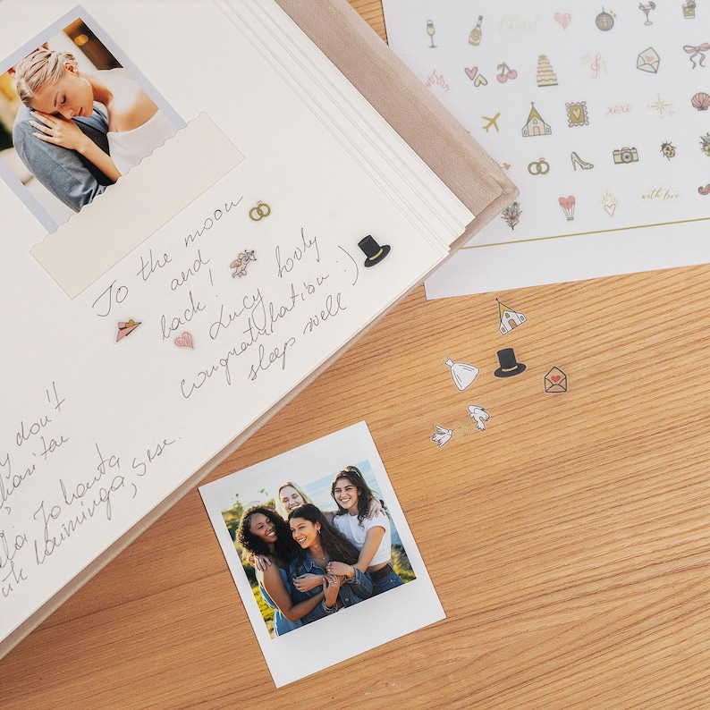 Pode incluir: Um &aacute;lbum de casamento aberto com uma foto de um casal e um polaroid de amigos. H&aacute; texto manuscrito e adesivos decorativos. Mais adesivos e uma superf&iacute;cie de madeira est&atilde;o espalhados.