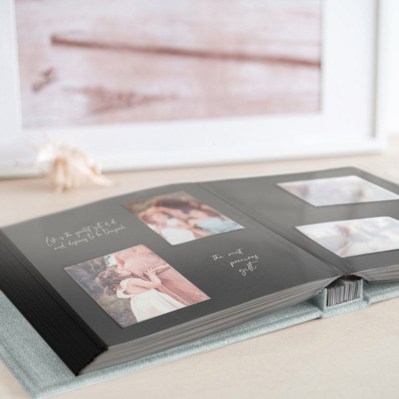 May include: Open photo album with gray pages and several photos. The album is open to a spread with two photos and text that reads "Life is the greatest gift and dispairing to be true good" and "the most precious gift". The album has a light blue cover.