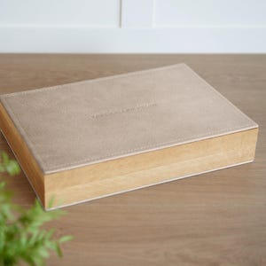 May include: A rectangular box with a light tan suede-like lid and a natural wood base. The lid has the text "VASLEY AND REIGN" embossed on it. The box is sitting on a wooden surface.