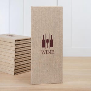 May include: A stack of beige linen-textured menu covers with a wine-themed logo. The logo features a wine glass and two bottles. The word "WINE" is printed below the logo in a dark brown color. The covers are stacked on a light brown wooden surface.