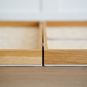 May include: Two wooden picture frames with light-colored wood and a white border. The frames are positioned side-by-side, with a small gap between them. The background is a light color, and the frames are on a wooden surface.
