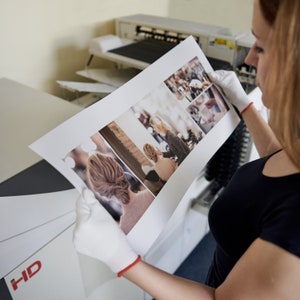 May include: A person is holding a printed photo collage with multiple images of people. The photo is printed on a white background and has a glossy finish.