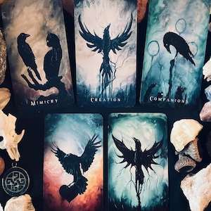 May include: A collection of tarot cards with dark, artistic illustrations. Each card features a raven or crow with symbolic imagery and titles like "Mimicry," "Creation," and "Shapechanger." The color palette includes blues, blacks, and reds, creating a mystical aesthetic.