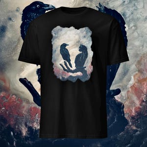 May include: Black t-shirt with a graphic of a crow and a cat sitting on a branch in a watercolor-style design.