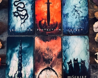 May include: Six tarot cards with mystical illustrations and text. The cards feature images of a snake, sword, tree, and cats, with words like "Seduction," "Protection," and "Mischief." The color palette includes blues, oranges, and blacks.