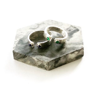 May include: Two silver rings with embedded gemstones. One ring has a green gemstone and the other has a blue gemstone.
