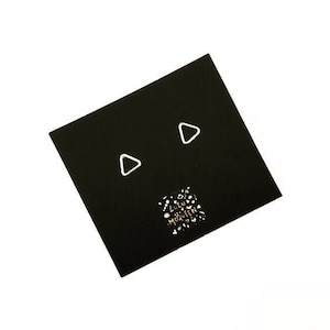 May include: A pair of silver triangle earrings on a black card with the text "Lulu McQueen" in gold lettering.