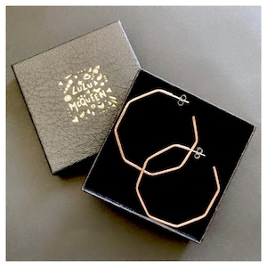 May include: A pair of rose gold octagon hoop earrings in a black velvet box with the text "ZULU McQUEEN" in gold lettering.