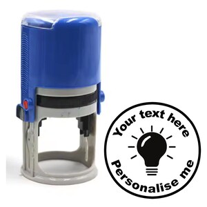 May include: A blue self-inking stamp with a clear plastic top. The stamp features a black light bulb icon and the text "Your text here Personalise me".
