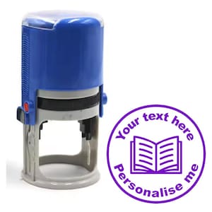 May include: A blue self-inking stamp with a clear plastic top. The stamp features a purple circle with the text "Your text here Personalise me" and an open book icon.