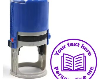 Könnte beinhalten: Ein blauer Stempel mit Selbsttinte und einem transparenten Plastikdeckel. Der Stempel zeigt einen violetten Kreis mit dem Text "Your text here Personalise me" und einem offenen Buchsymbol.