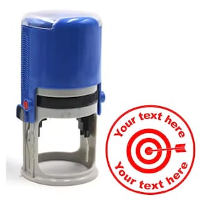May include: A blue self-inking stamp with a clear plastic top. The stamp features a red target with an arrow and the text "Your text here" around the target.