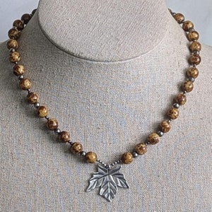 May include: A brown and gold beaded necklace with a silver maple leaf pendant.