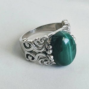 May include: A silver ring with a green malachite stone set in a filigree design. The ring is marked "INDIA" on the inside band.