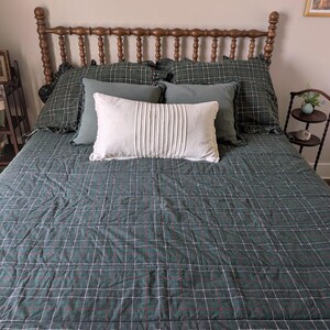 Peut inclure: Un lit avec une tête de lit en bois et une courtepointe à carreaux verts. Le lit est fait avec des oreillers à carreaux verts et un oreiller décoratif blanc. Une petite table de chevet et une bibliothèque sont visibles en arrière-plan.