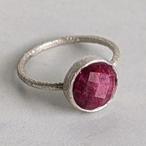 May include: A silver ring with a textured band and a red gemstone set in a bezel setting.