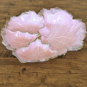 Op de afbeelding: Een roze, bladvormige serveerschaal met witte aderen en een goudkleurige rand. De schaal is gemaakt van keramiek en heeft een glanzende afwerking. De schaal is ontworpen om meerdere items te bevatten.