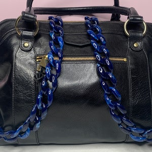 May include: Black leather handbag with a blue plastic chain strap. The bag has a gold zipper and gold hardware.