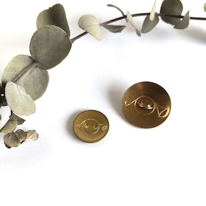 May include: Two gold-coloured buttons with a raised design. The larger button has a simple design, while the smaller button has a face with two eyes and a smile.