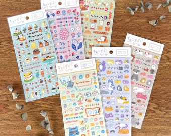 Op de afbeelding: Een verzameling sticker vellen met diverse ontwerpen. Eén vel toont illustraties van eten en drinken, een ander heeft bloempatronen, en andere tonen dieren en briefpapier. Elk vel heeft Japanse tekst bovenaan.