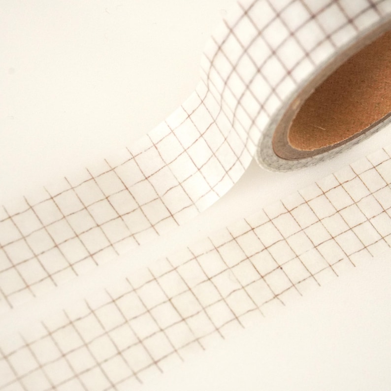 May include: A roll of white washi tape with a brown grid pattern. The tape is partially unrolled, showing the grid pattern.