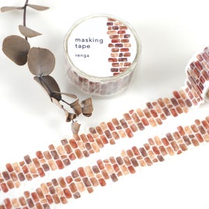 May include: A roll of washi tape with a brick pattern. The tape is red, orange, and brown. The text on the roll says "masking tape renga".