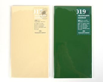 May include: Two Traveler's Company notebooks. One is cream-coloured, labelled "017" with Japanese text and "Free Diary (Monthly)". The other is green, labelled "019" with Japanese text and "Free Diary (Weekly+Memo)". Both are in clear plastic.