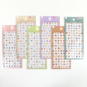 Op de afbeelding: Zeven stickervellen met diverse ontwerpen, waaronder eten, bloemen en alledaagse voorwerpen. De stickers zitten in een transparante plastic verpakking met geschulpte randen. Het kleurenpalet omvat roze, groen, paars en bruin.