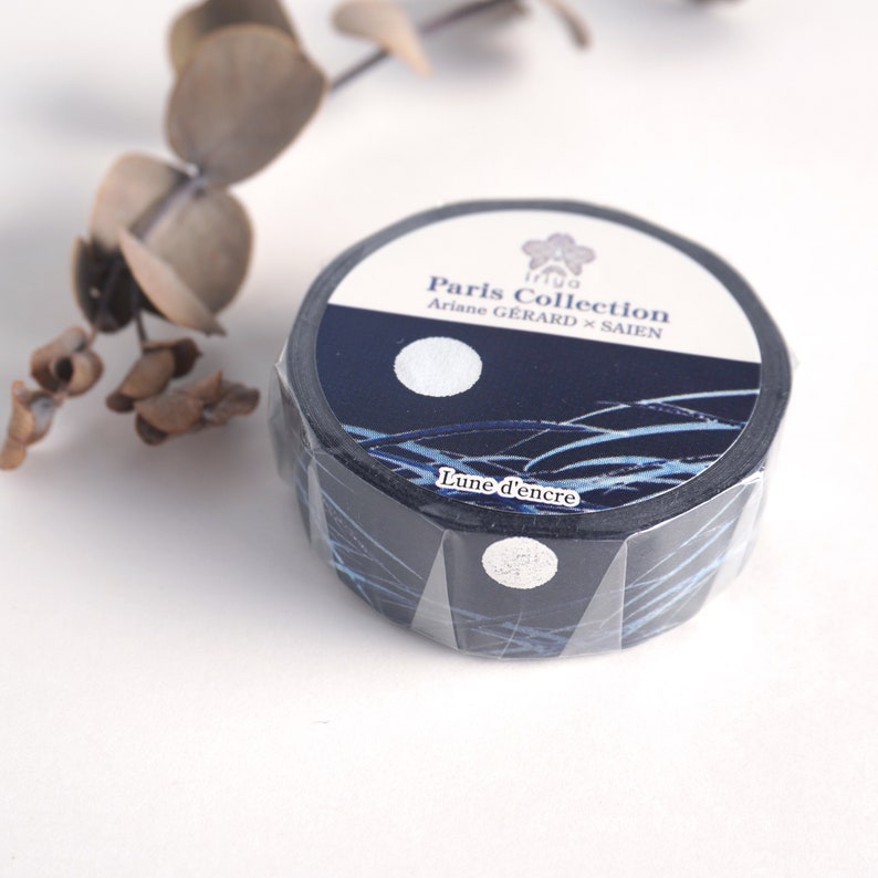 Może przedstawiać: Rolka czarno-niebieskiej taśmy washi z wzorem księżyca i fal. Taśma jest oznaczona "Paris Collection Ariane GERARD x SAIEN Lune d'encre".