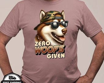 May include: A mauve t-shirt featuring a cartoon husky wearing sunglasses and a camouflage cap. The text "ZERO WOOFS GIVEN" is printed below the dog's image in a retro font. The dog has a gold chain.