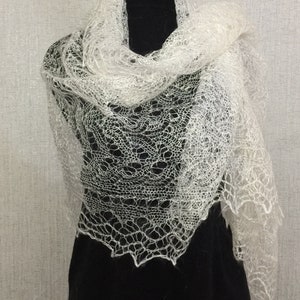 以下が含まれることがあります： 繊細で複雑なパターンが施された白いレースのショール。ショールは黒いマネキンにかけられています。