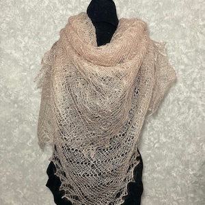 May include: A delicate, light pink lace shawl with a delicate, intricate pattern. The shawl is draped over a black mannequin.